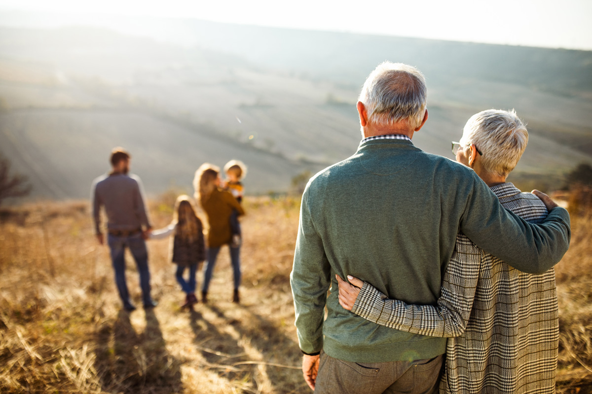 elderly couple watch their children and grandchildren playing on a beautiful day